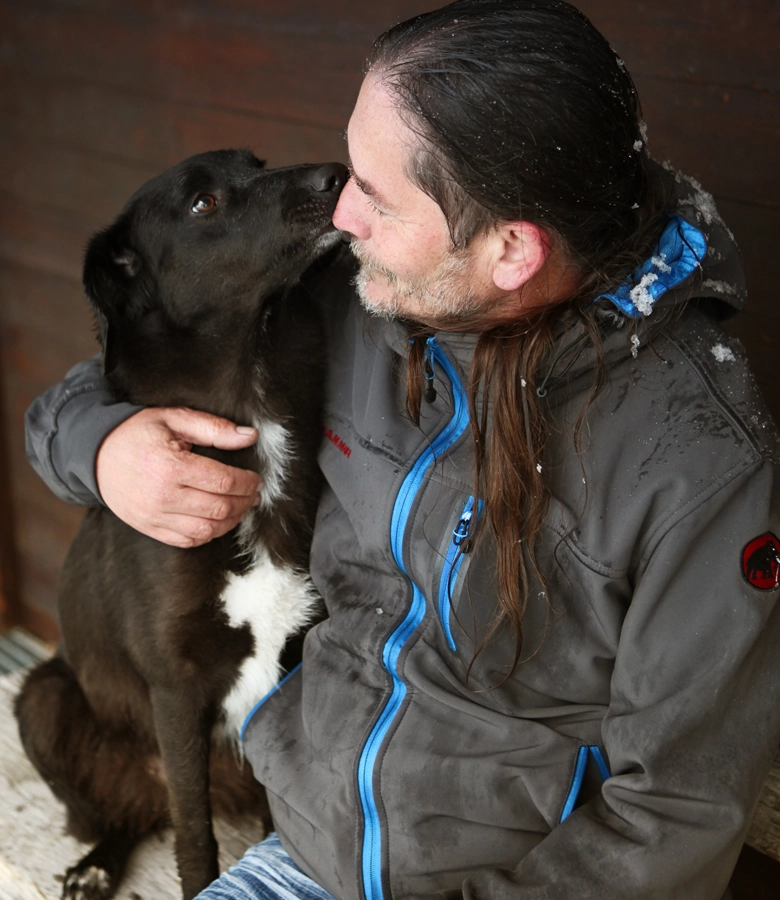 Herr Blickle sitzt auf einer bank und umarmt einen schwarzen Hund